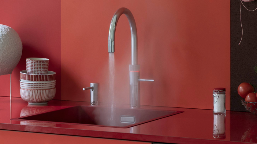 Quooker tap running steamy water into a sink with a red splashback and worktop