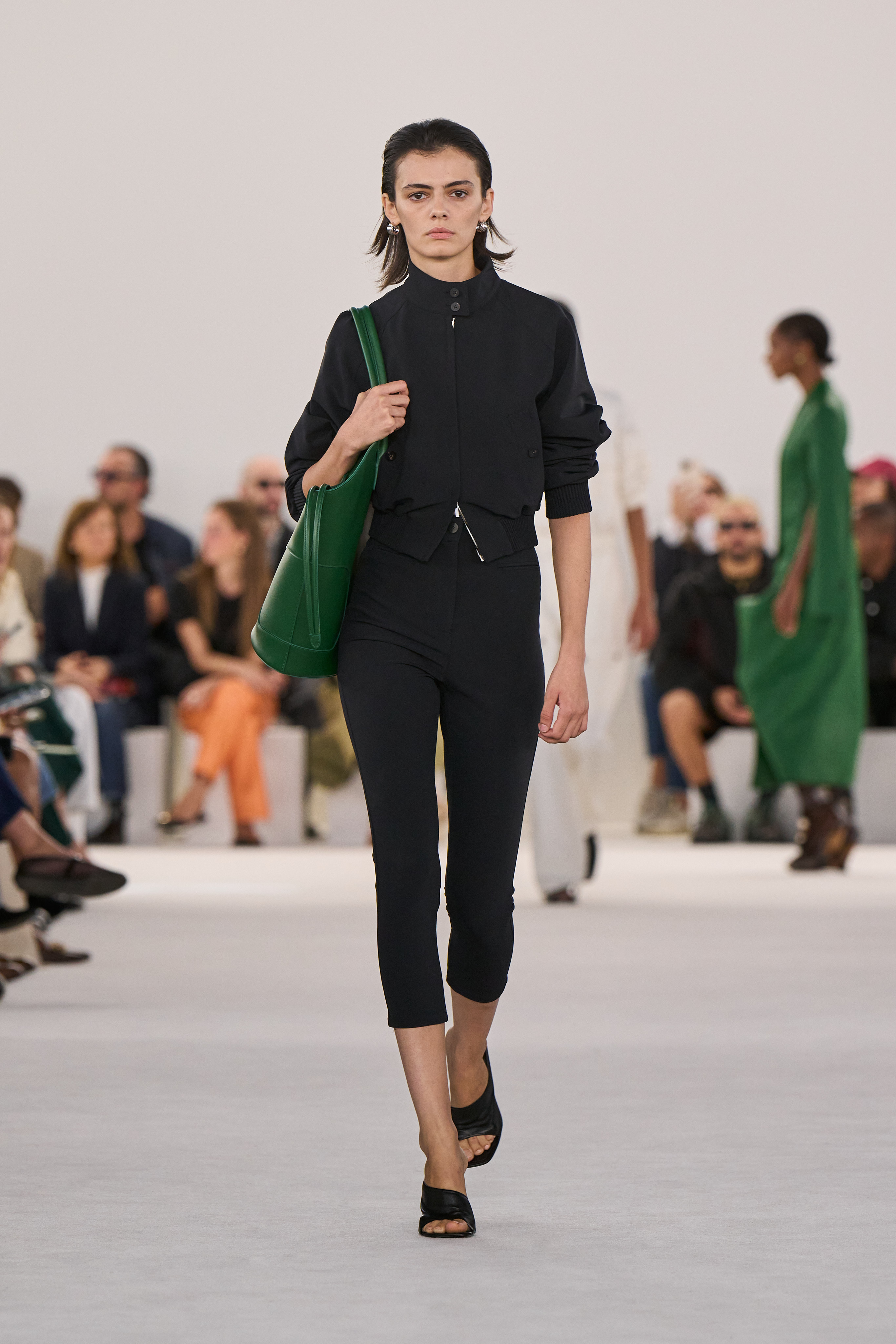 A Ferragamo model wearing a black cropped jacket and cropped leggings on the runway.