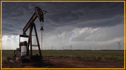 A close up of an oil rig with wind turbines in the background.