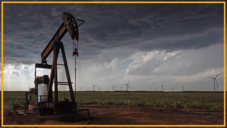 A close up of an oil rig with wind turbines in the background.