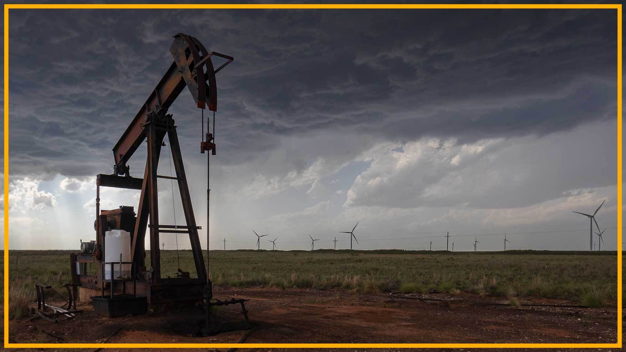 A close up of an oil rig with wind turbines in the background.