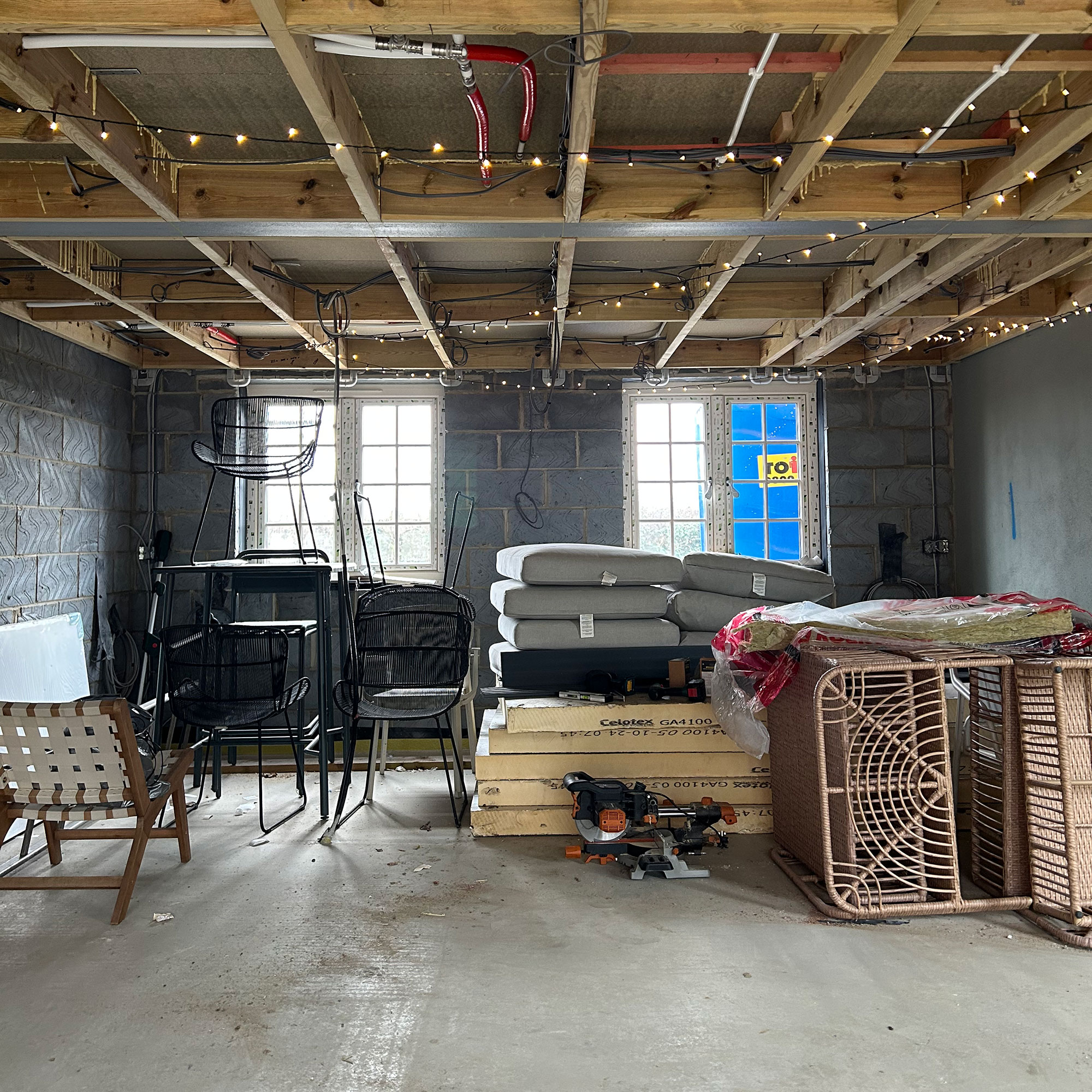 Open plan kitchen area in construction phase with piles of furniture and fairy lights on beams
