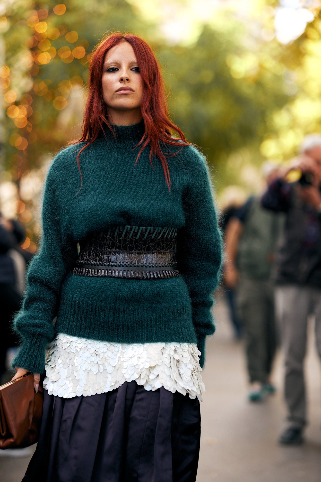 a woman with fiery red hair wearing a dark green sweater and black belt