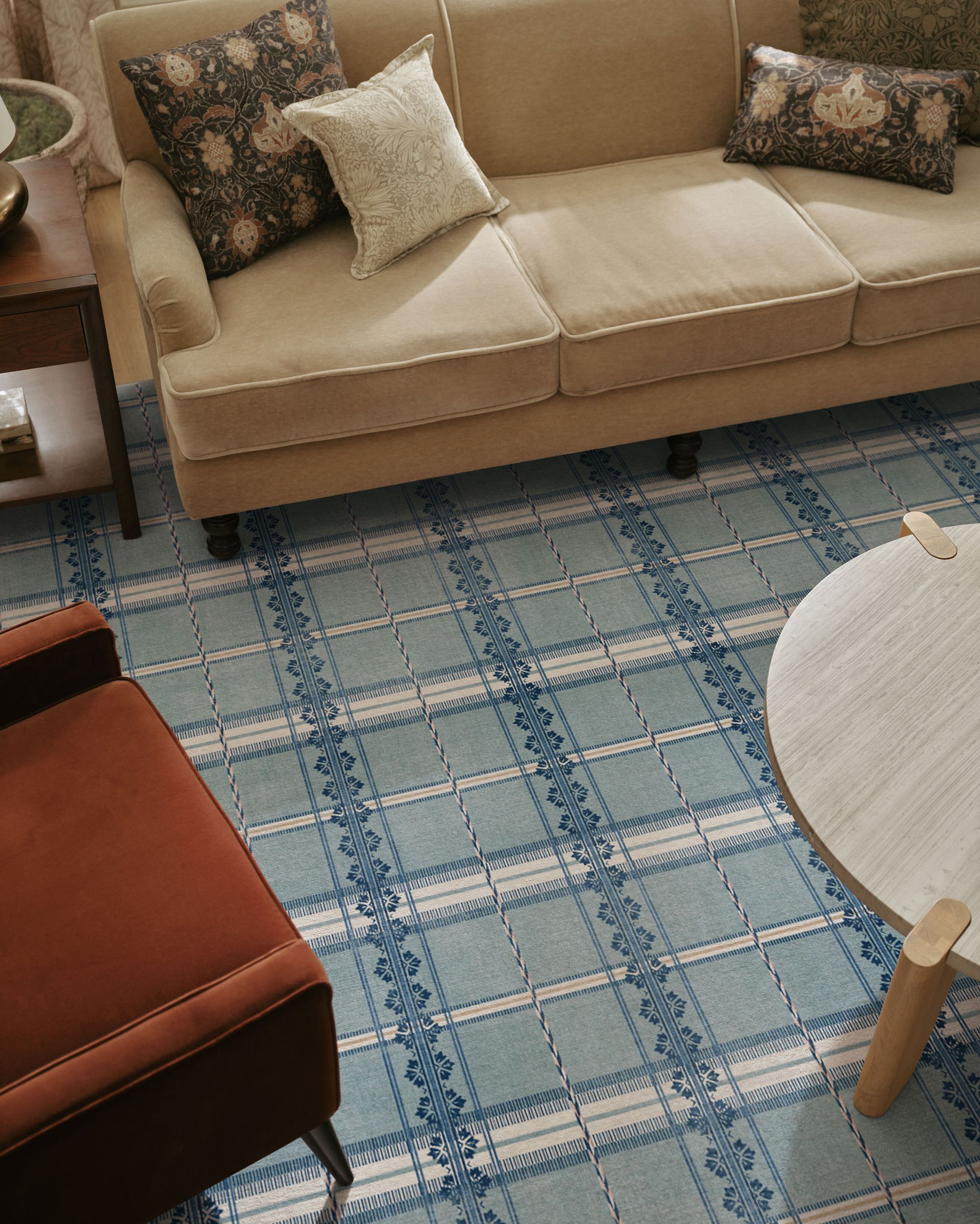 Image from above of a light blue and white checkerboard-inspired rug with a beige sofa, a wooden coffee table, and a rust orange accent chair on it.