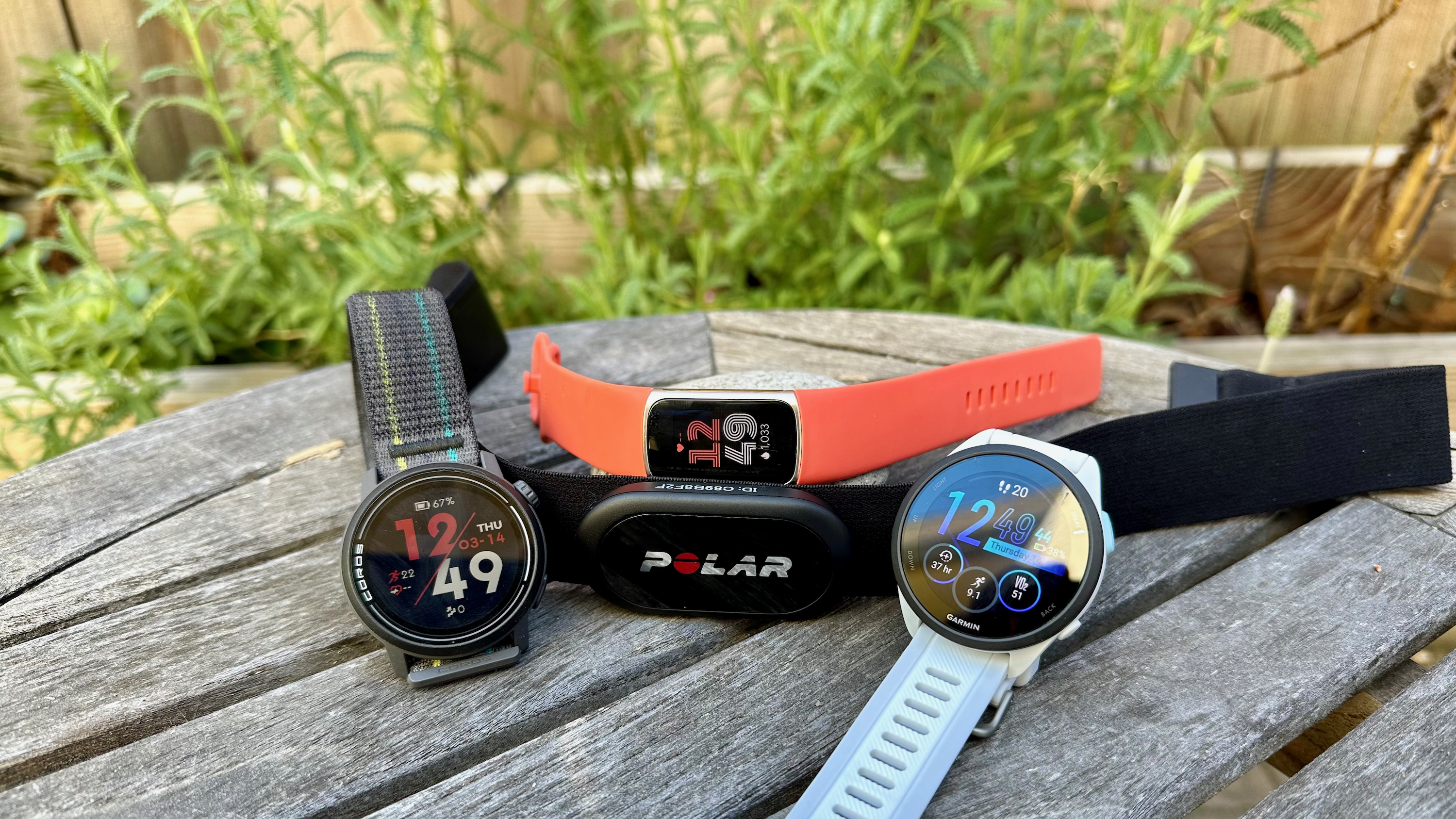 The Garmin Forerunner 165, COROS PACE 3, Fitbit Charge 6, and Polar H10 sitting together on a table.