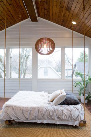 rustic bedroom with shiplap walls and ceiling, bed hanging from ropes, coir rug, bent wood ceiling light