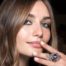 Two models with their hands laid against the cheeks showing off their milky white nail polishes. 