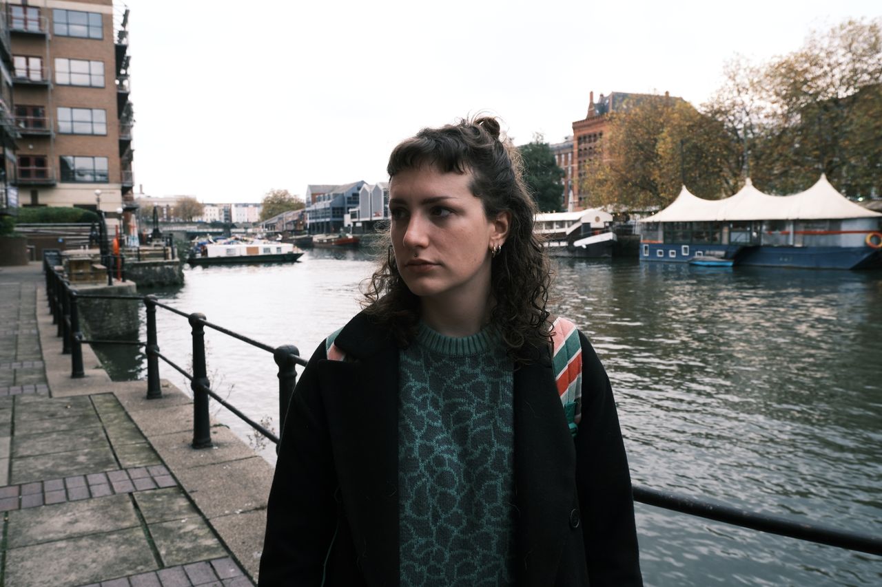 A portrait of a woman with curly hair with water in the background, taken on a Fujifilm X-M5 mirrorless vlogging camera