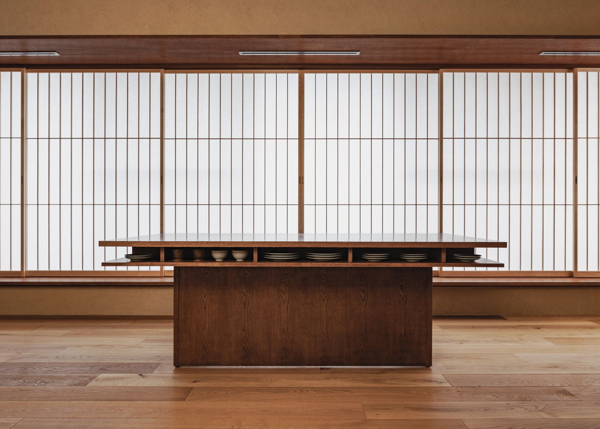 A wooden kitchen island stands solitary in front of multiple Japanese shoji screens with nothing on top and with an open storage section underneath to house plates and cups