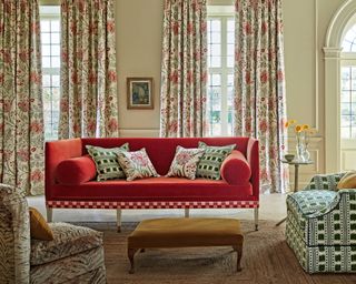 Living room with floral patterned curtains, red sofa with checkered trim, colorful armchairs and rug