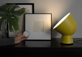 a yellow smart lamp on a black table next to pictures