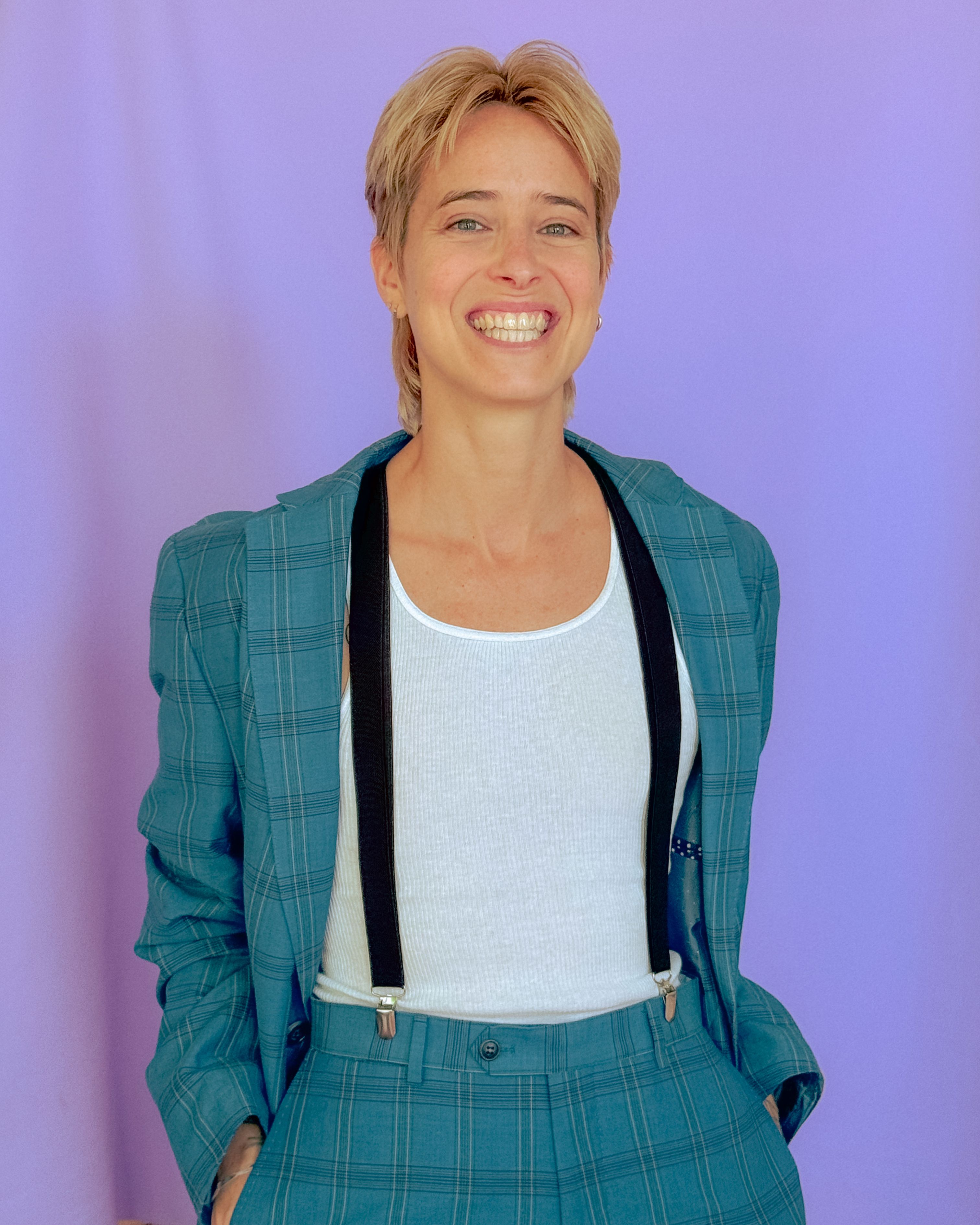 Two people dressed in colorful clothing stand against an electric lilac background while smiling to the camera.