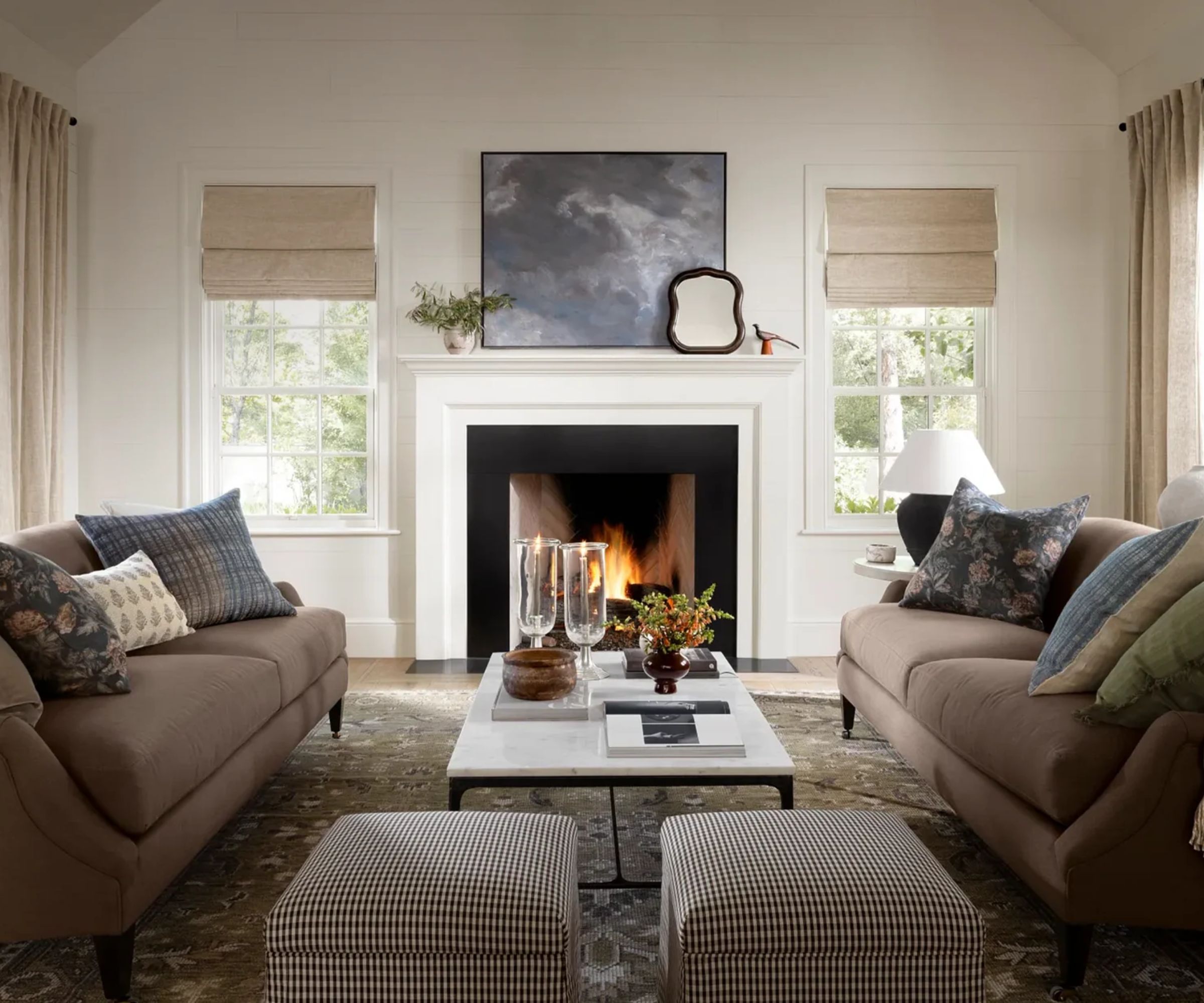 cozy neutral living room styled for fall using the mcgee and co fall 2025 collection. A large white fire is styled with a blue abstract painting, while two taupe sofas face each other styled with plaid and floral pillows and a marble coffee table with small plaid ottomans