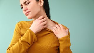 A woman scratching her neck while wearing a yellow jumper
