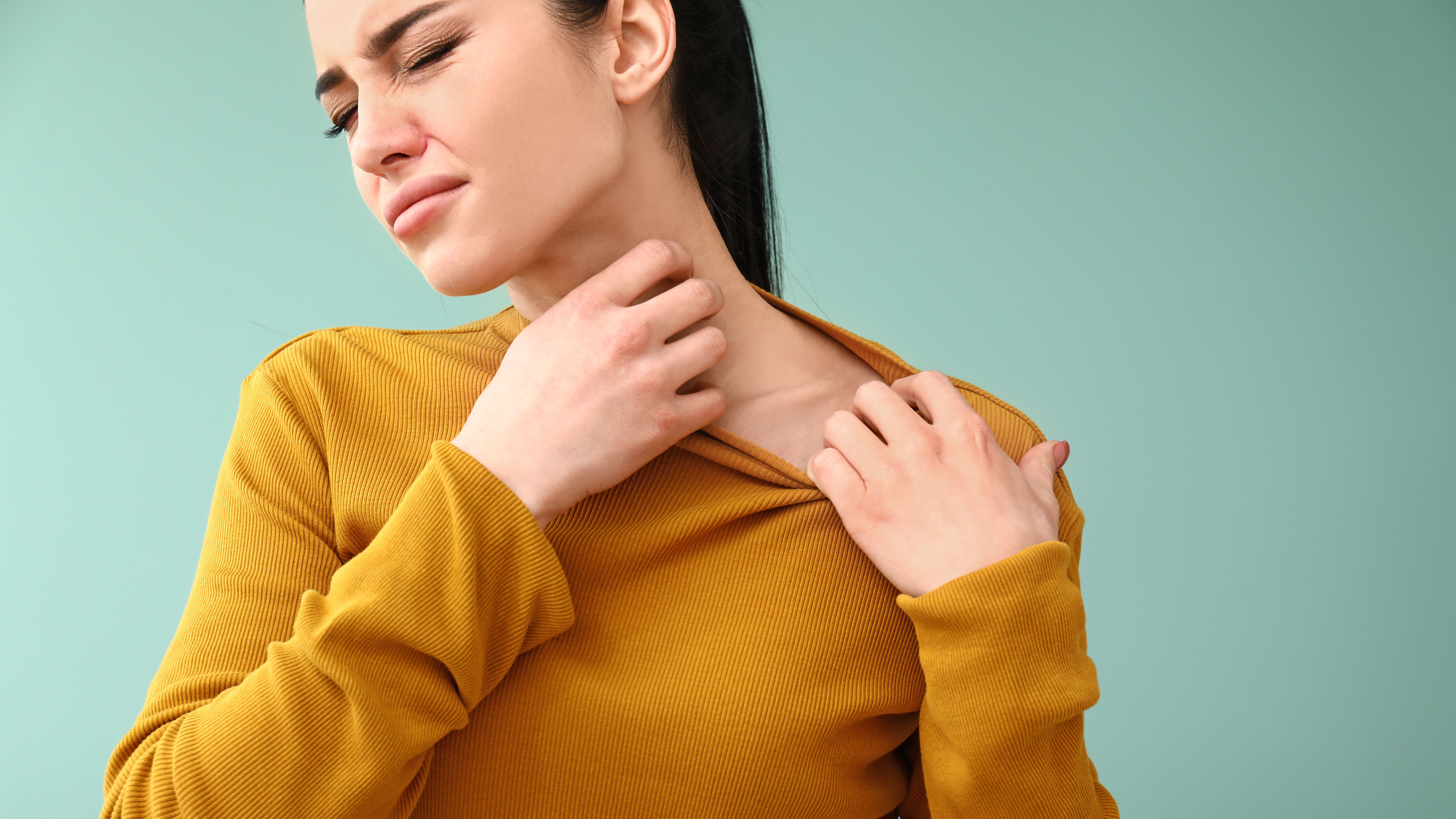 Eine Frau kratzt sich am Hals, während sie einen gelben Pullover trägt