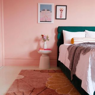 A pink bedroom with a dark green bedframe, art on the walls and a pink and yellow floral area rug