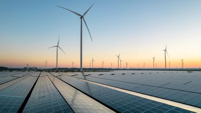Wind turbines and solar powers are seen outside as the sun sets.