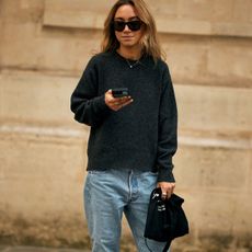 Woman in sweater and jeans looking at a phone