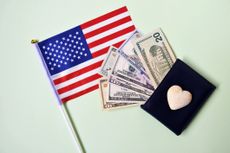 A wallet with a heart on it with money coming out onto an American flag