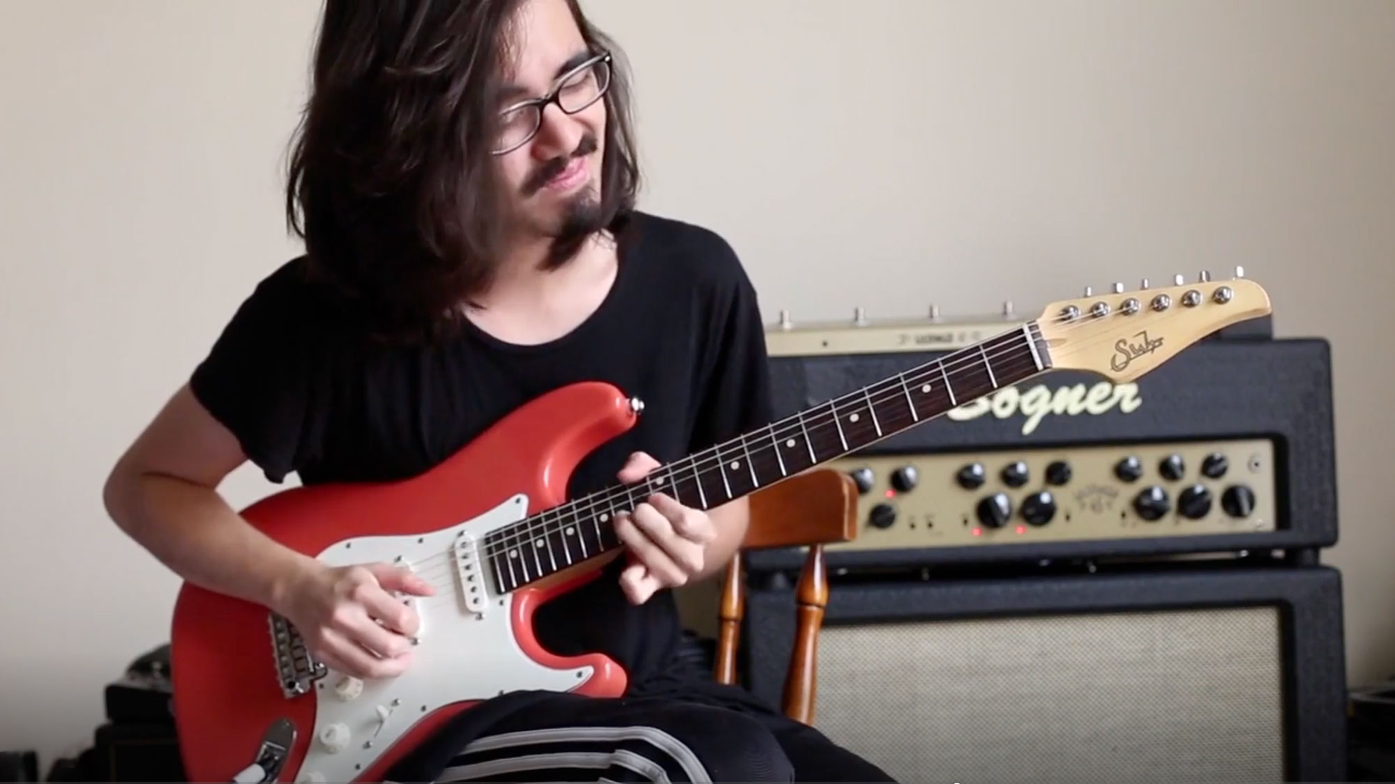 Mateus Asato plays a red Suhr Stratocaster-style guitar.