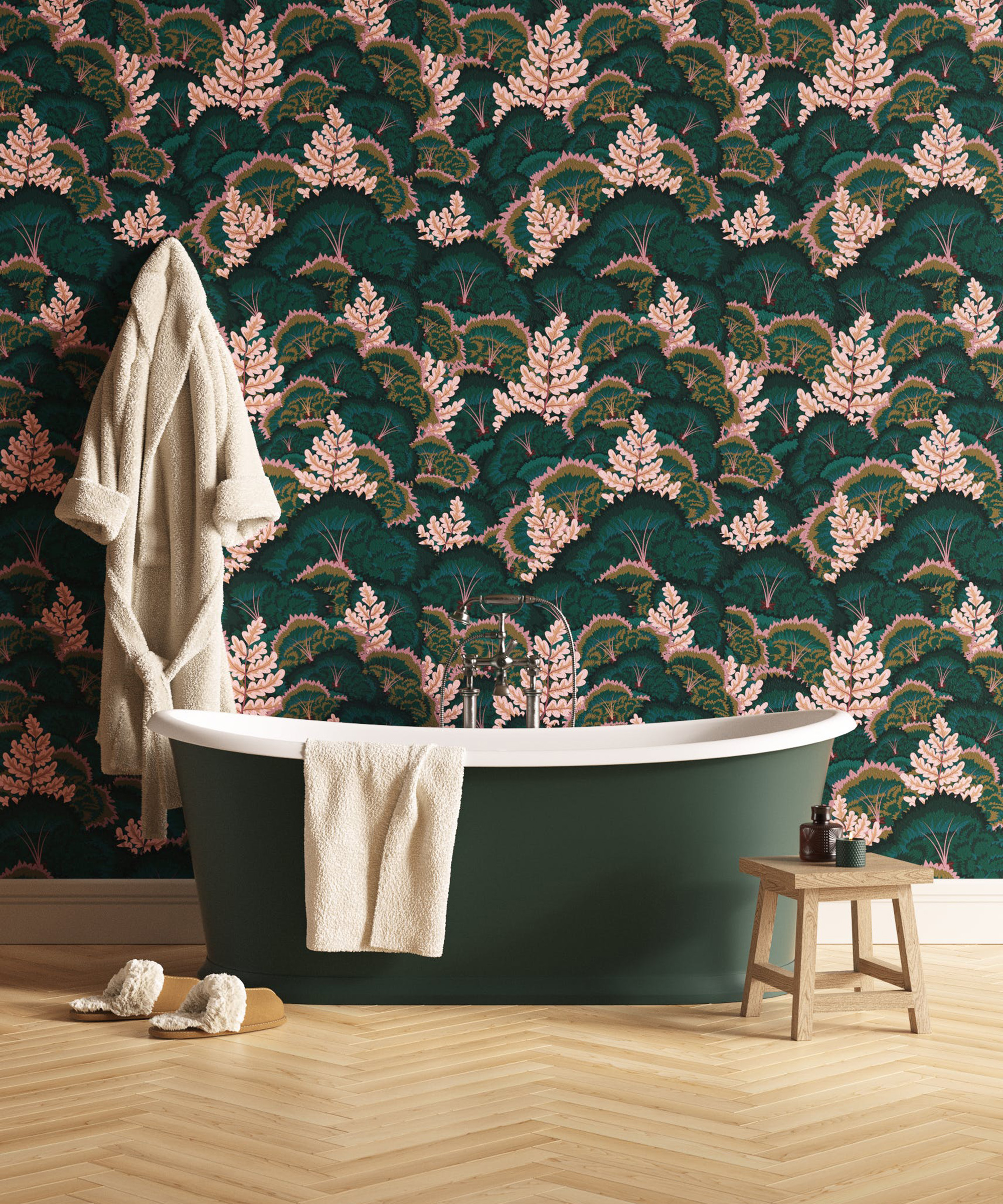 A dark green free-standing bath on herringbone flooring in front of bold green and pink wallpaper