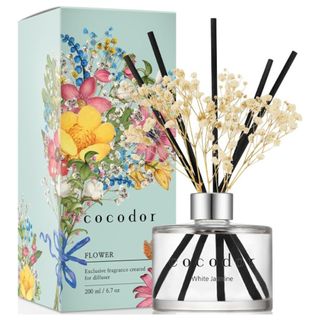 A reed diffuser with black reeds and white baby's breath flowers with a blue cardboard packaging box covered in a colorful bouquet of flowers