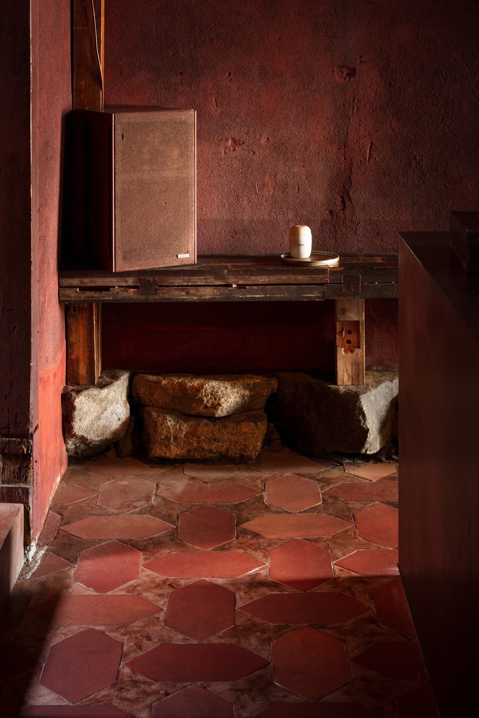 A terracotta-tinted cafe and bar with large, poligonal tiles on the floor, neon lights and sconces, wooden beams and furniture, and a dimly lit ambiance.