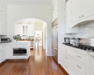 A kitchen with white cabinets, marble backsplash and wooden floors