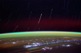 star trails arch upward from behind the cuve of earth, streaking its lights below, with a then veil of atmosphere at its crown.