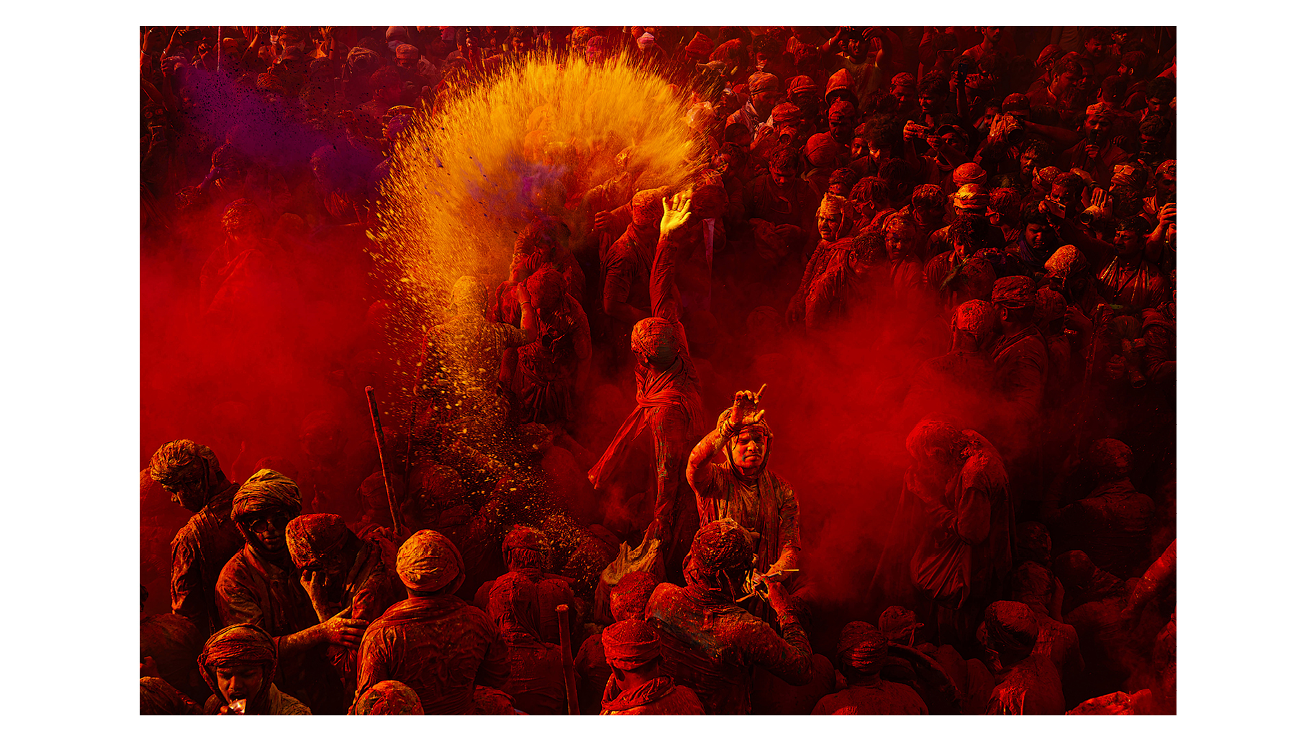 Photograph of a vibrant moment from the Holi festival in Mathura, Uttar Pradesh, India, showing a striking burst of yellow powder filling the air among a sea of red, taken by Tittu Shaji Thomas, and the Runner-Up in the One Shot: Festivals & Celebrations category of Travel Photographer of the Year 2024