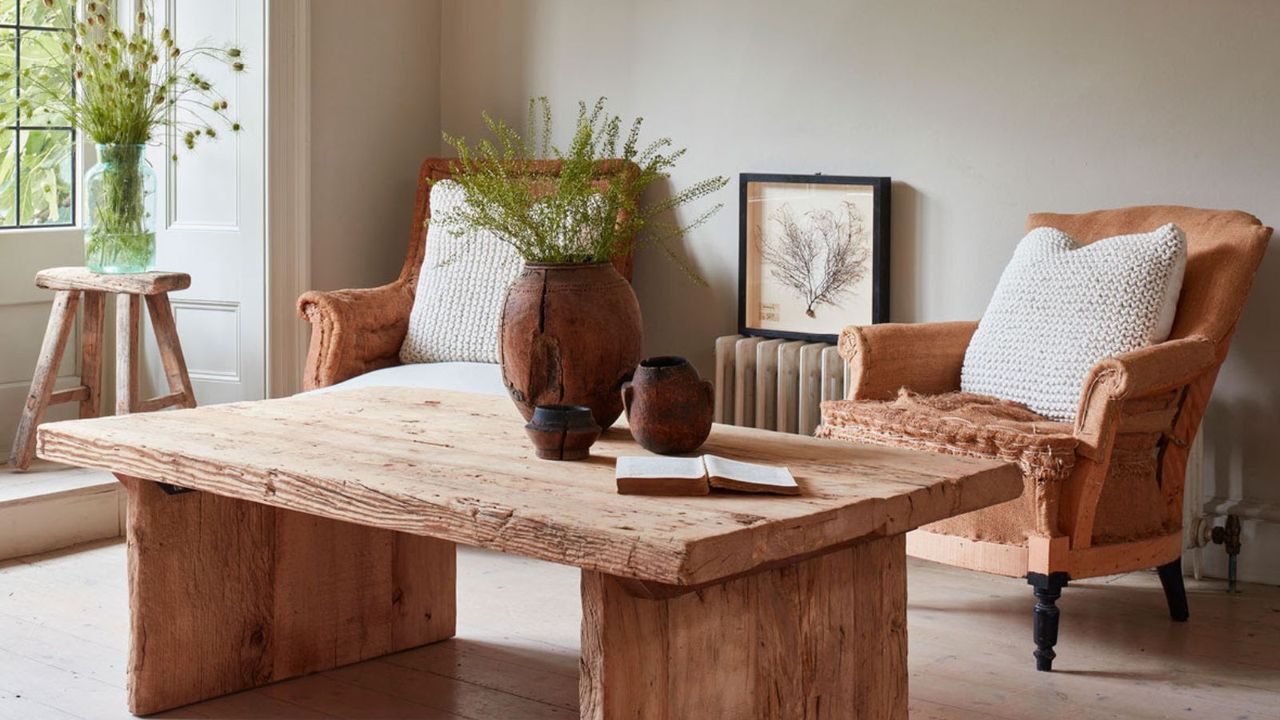 A living room with a small radiator between two plush arm chair , behind a rustic wooden table