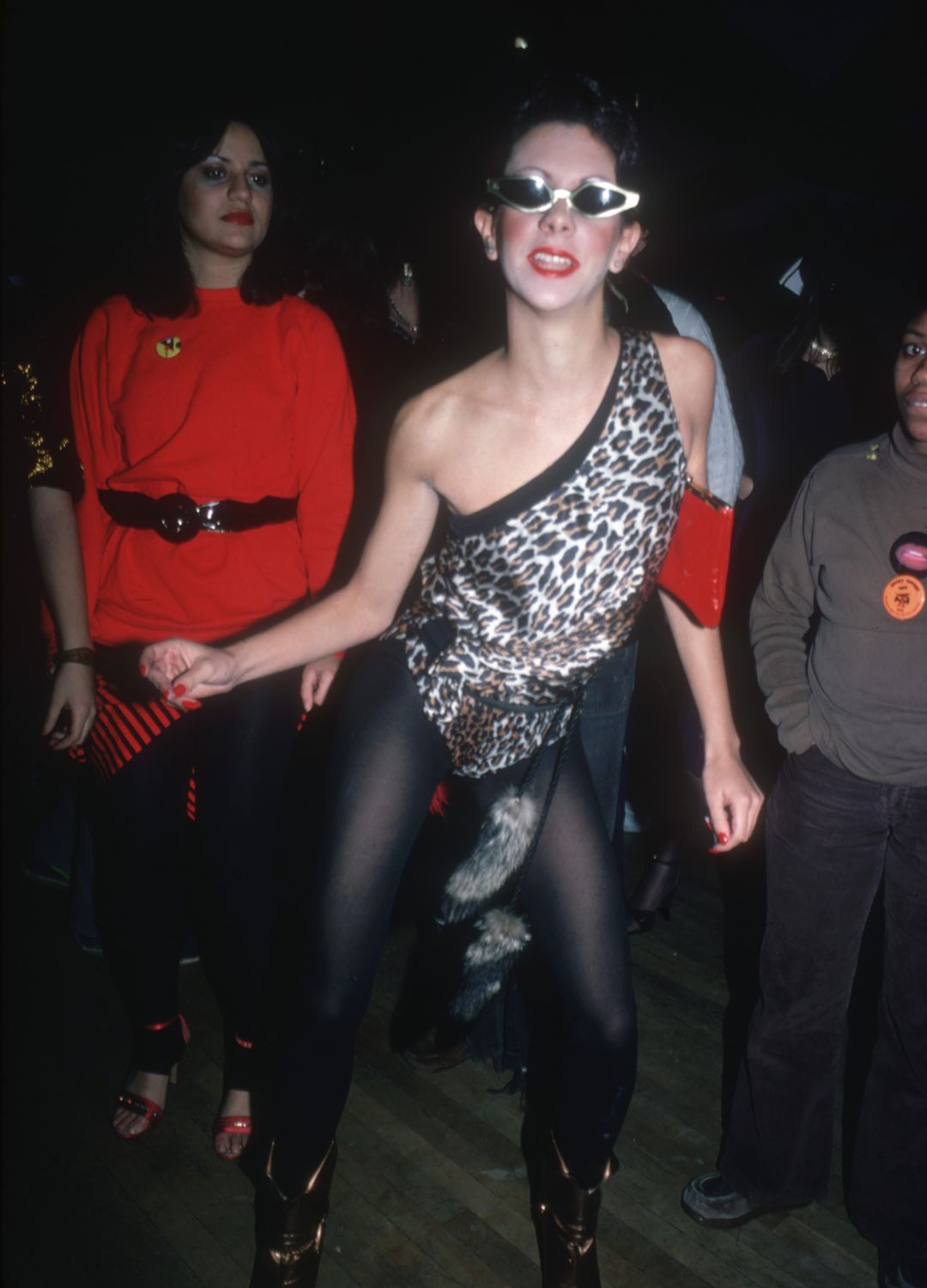 Portrait of an unidentified party-goer, dressed in boots, black tights, a sleeveless leopard-print, single shoulder top, and sunglasses at the nightclub Studio 54, New York
