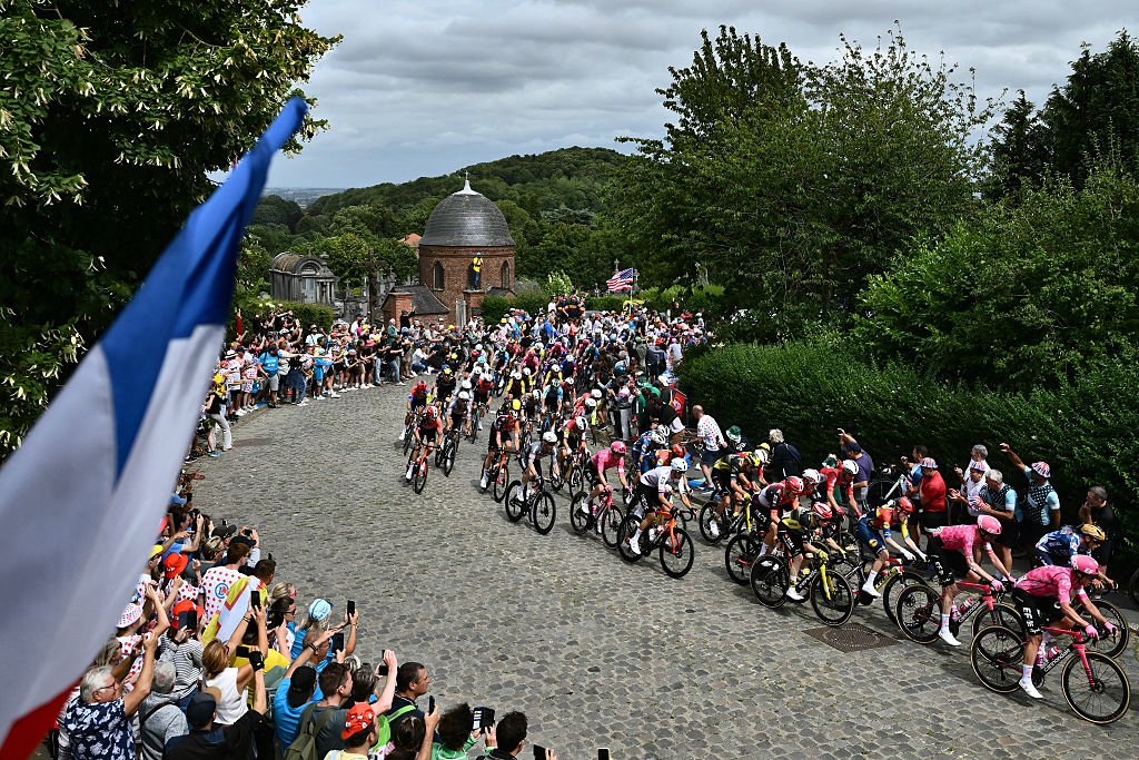 The pack of riders (peloton) cycles over a cobblestone sector in Cassel during the 1st stage of the 112th edition of the Tour de France cycling race, 184.9 km starting and finishing in Lille Metropole, northern France, on July 5, 2025. (Photo by Marco BERTORELLO / AFP)