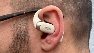 A close-up of one Shokz OpenFit 2 earbud in the reviewer's left ear