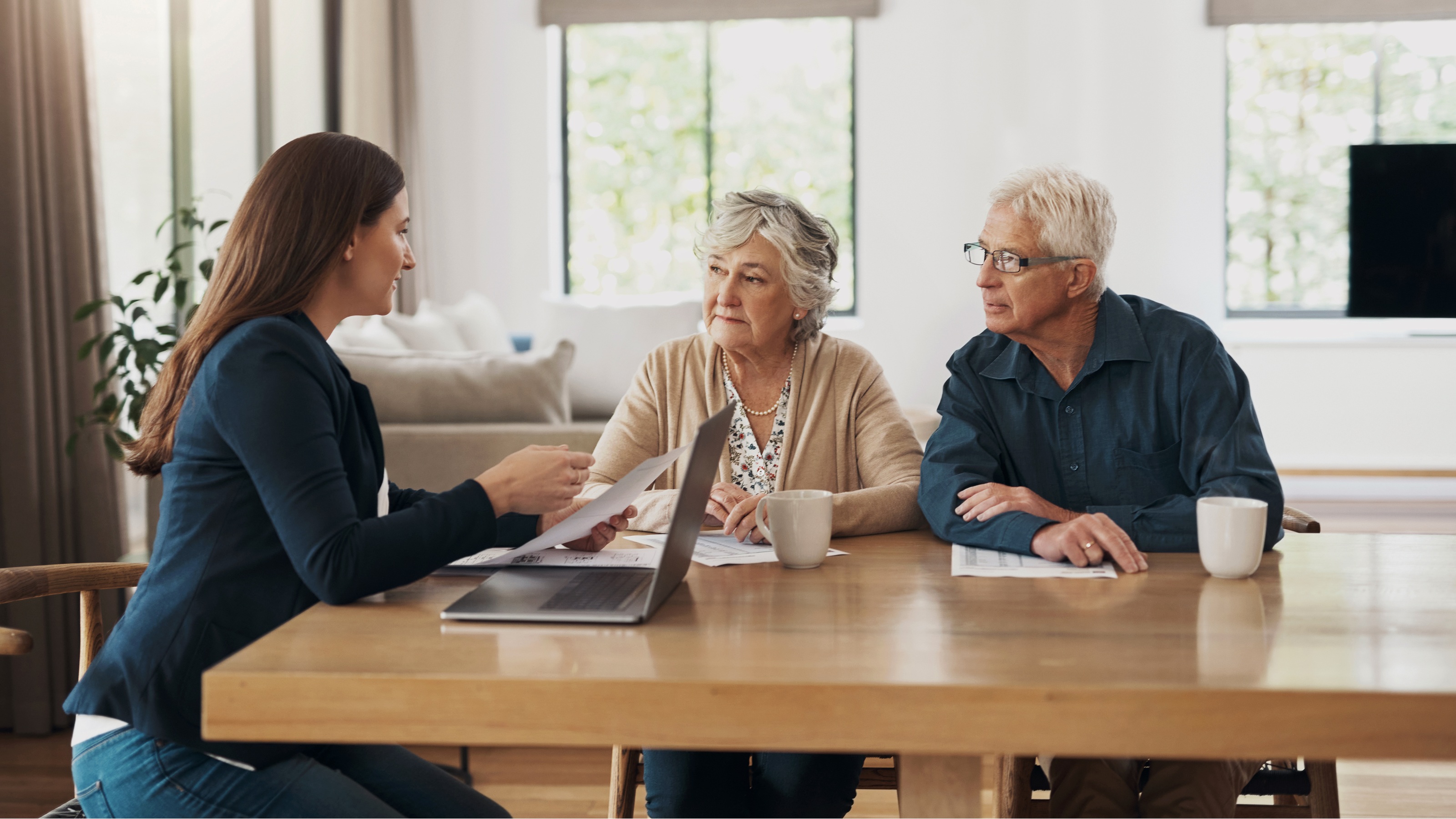 A financial adviser answers an older couple's questions at a conference room table.