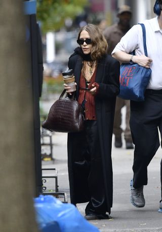 Mary-Kate Olsen wearing black pants, a red top, a black coat, and a black scarf with her hair tucked underneath in New York City on October 17, 2022.