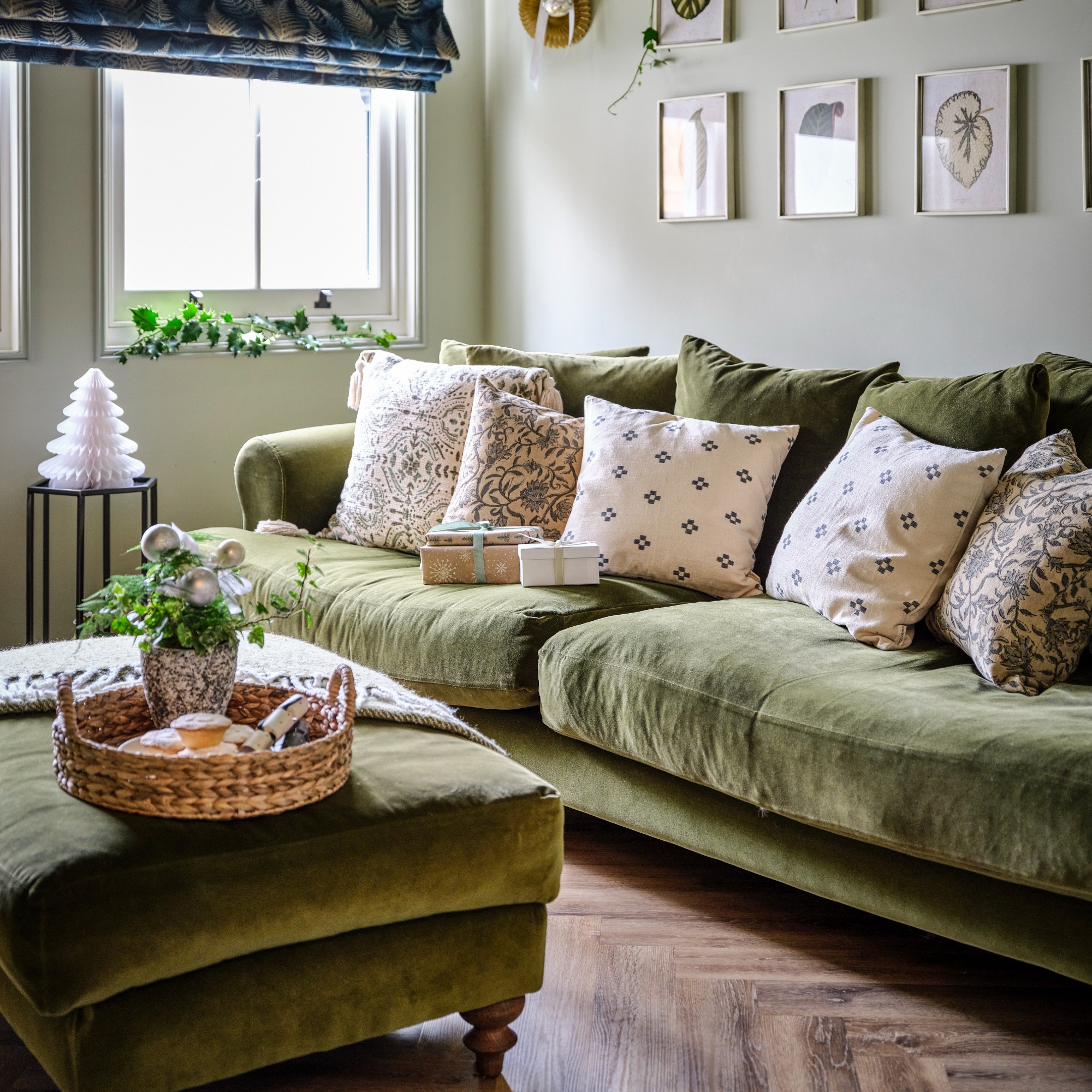A living room with a green velvet 3-seater sofa with a matching ottoman decorated for Christmas