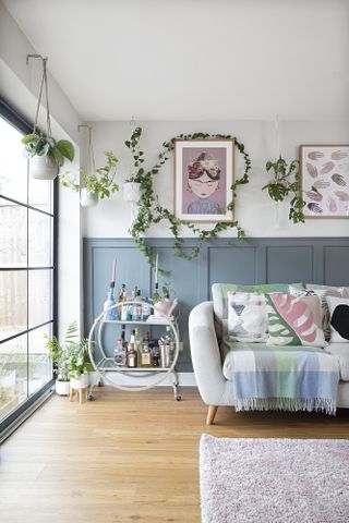 Snug area of open-plan space with blue panelling to dado height, light grey sofa, bar trolley and Crittal-style uPVC doors