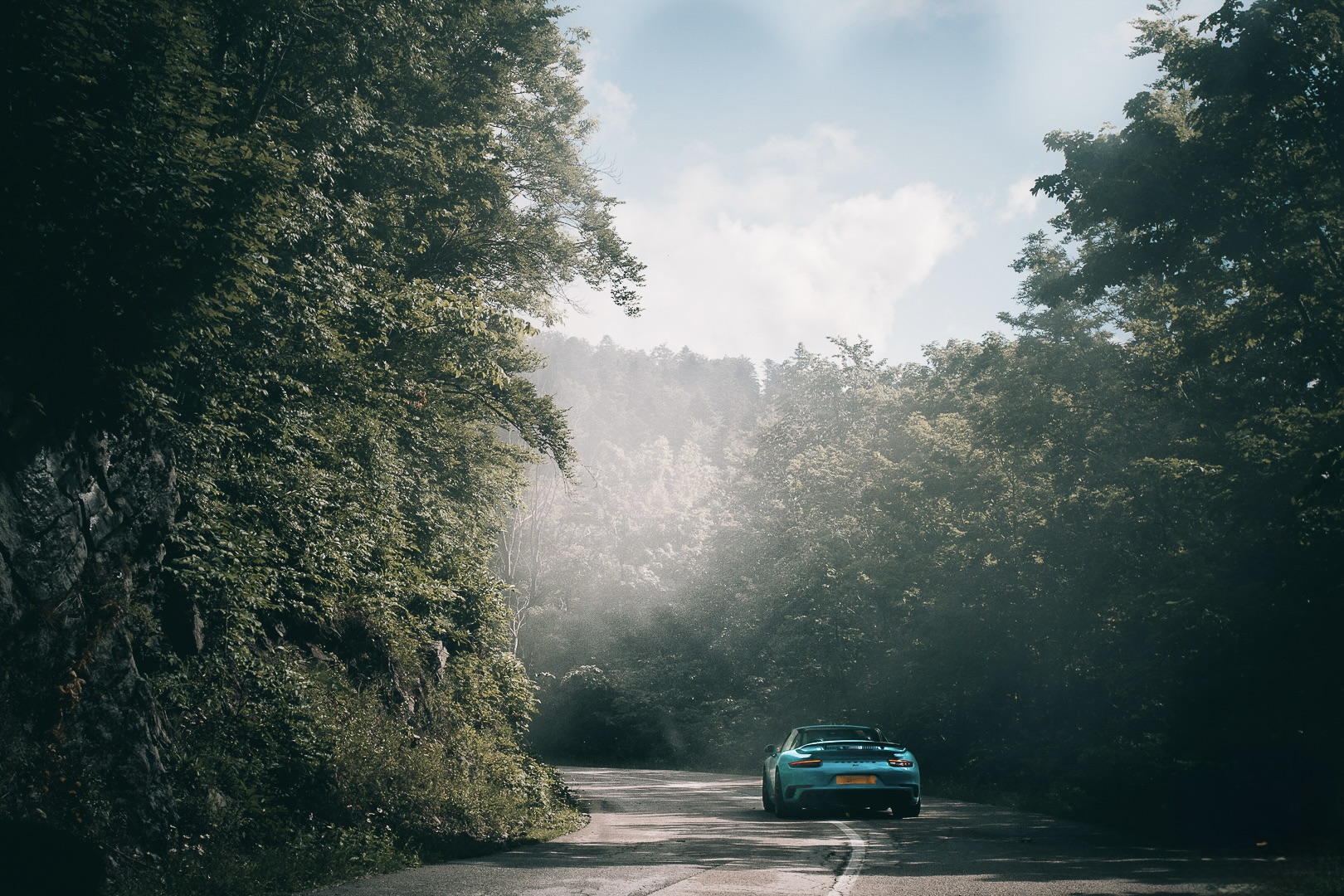 A porsche disappears down a road into some jungle