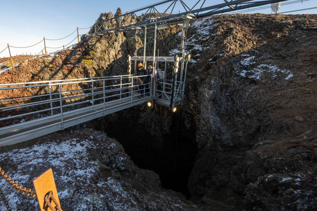 At the top of a volcano in Iceland, people stand in an elevator that will take them into the empty magma chamber below.