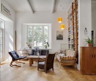 An open plan living room in a renovated school house with home library against the wall and two off-center ceiling lights