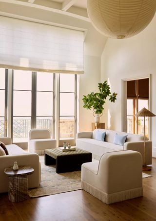 High ceiling, neutral living room with white fringe sofas and accent chairs