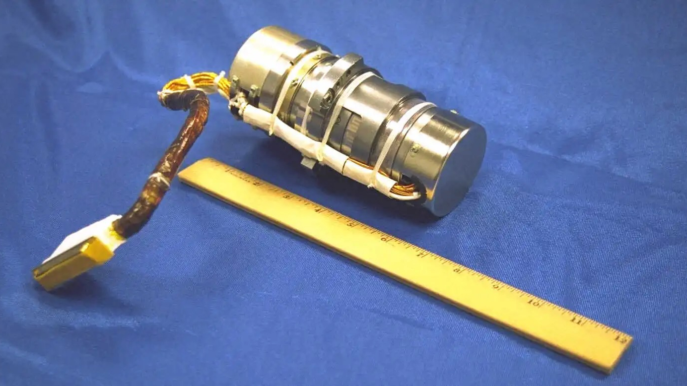 a silver metallic device on a blue tablecloth, with a yellow ruler in front of it