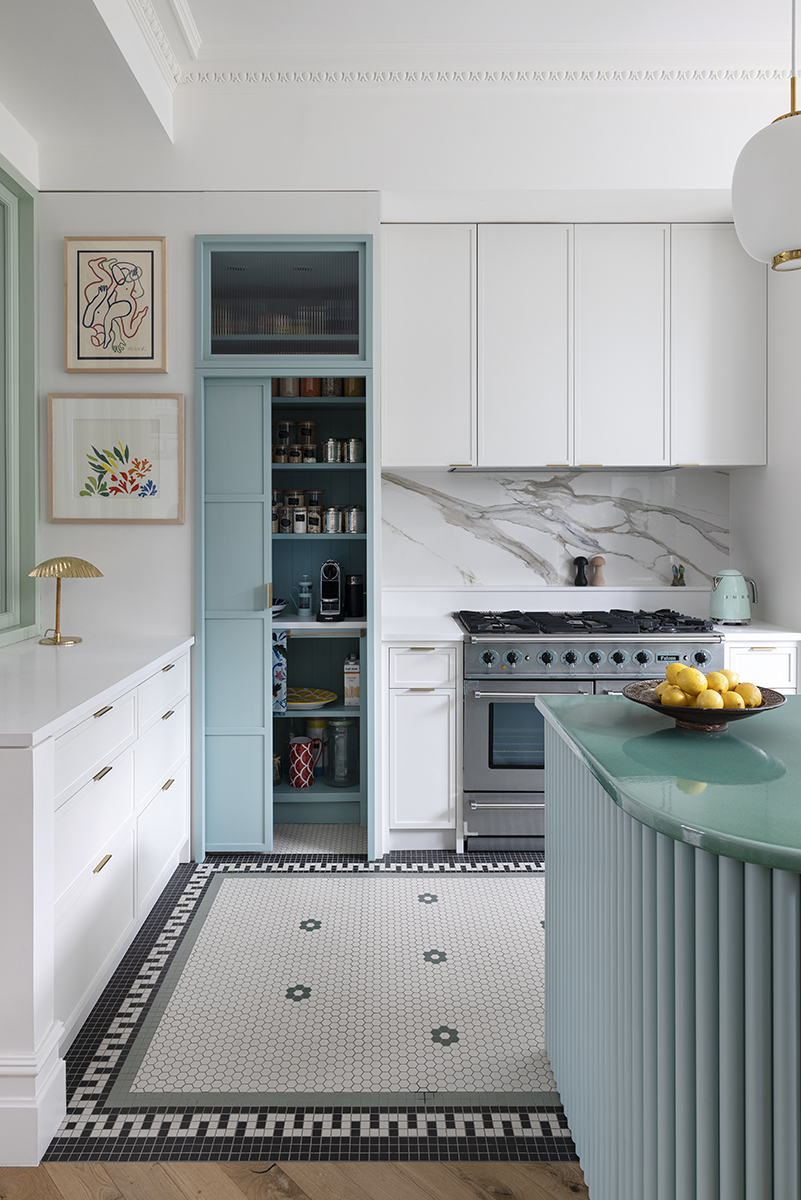 A small kitchen with blue island, patterned flooring and a slim profile pantry