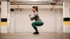 Woman in sportswear performs a squat in an underground parking lot