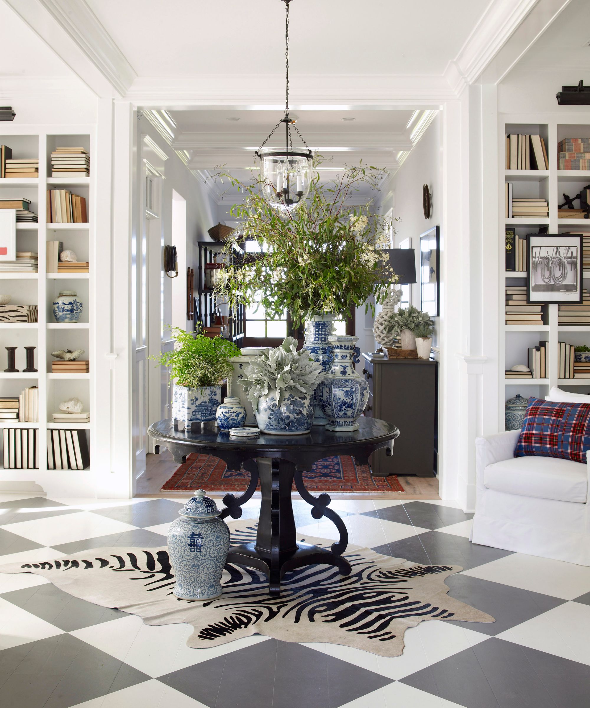 Entryway with checkerboard tiled floor, round antique table, blue and white pottery and bookshelves