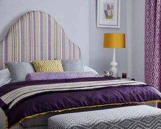 Lilac painted bedroom with large bed side table and purple curtains