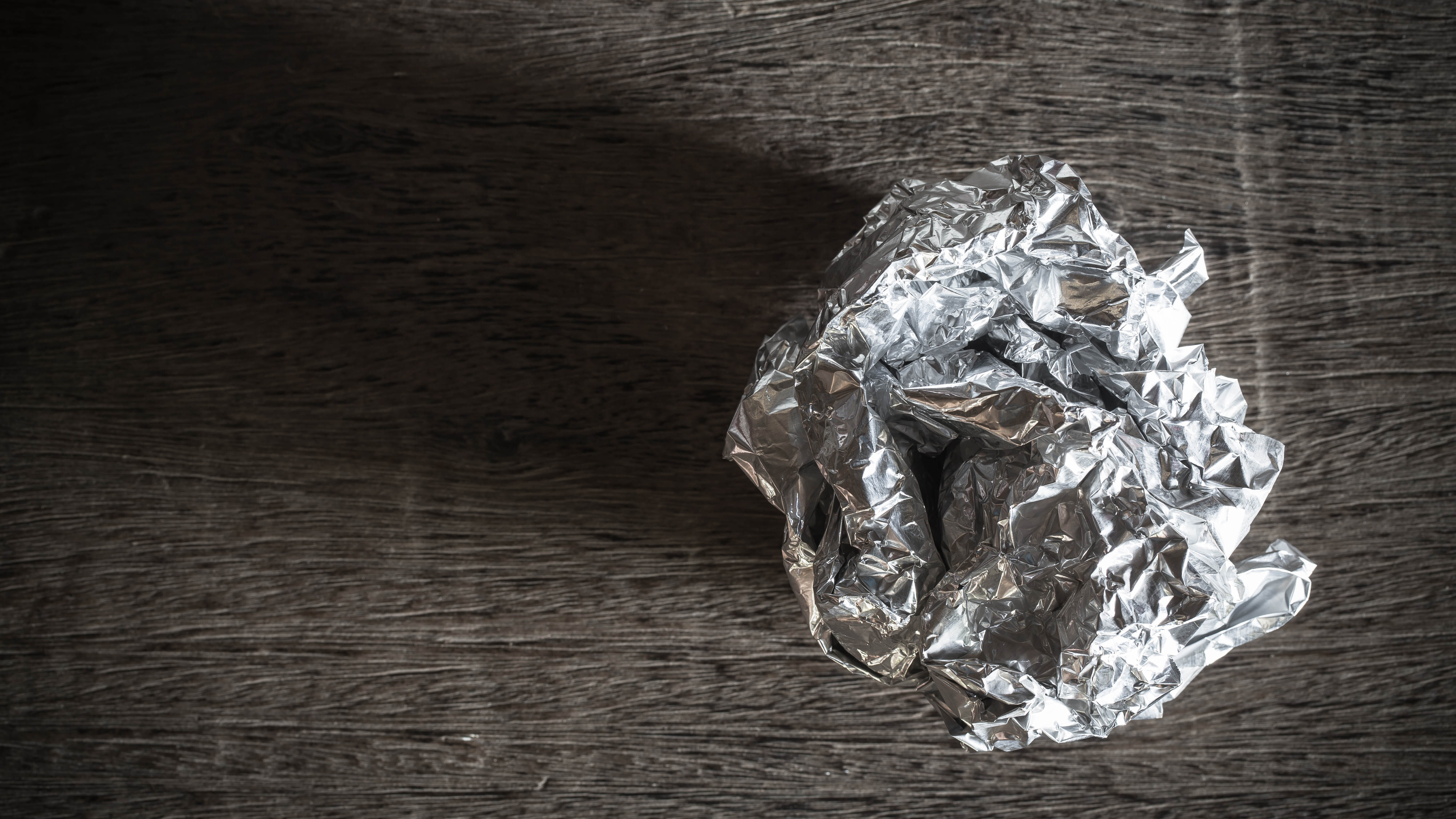 Aluminium foil scrunched up in a ball on a brown worksurface