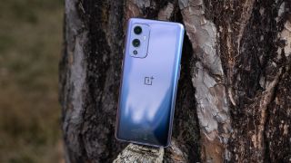 A OnePlus 9 from the back, leaning against a tree