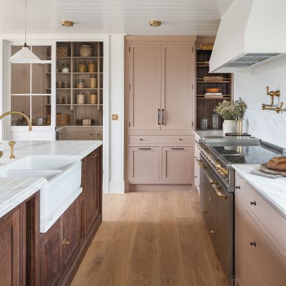 Shaker style kitchen with blush pink cabinets, wood island with sink, marble countertops, engineered wood flooring, white woodwork and shiplap style painted white ceiling, pantry 